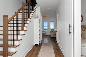 A modern interior with a wooden staircase, white walls, and a view to the outside. - West Wind (Port St. Joe)