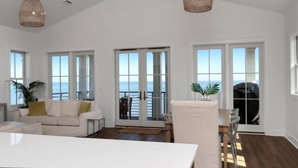 A spacious living room with a large white sofa, a dining table, and a view of the ocean through large windows. - West Wind (Port St. Joe)