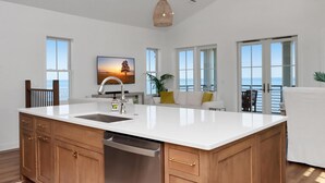 A spacious kitchen with a large island, wooden cabinets, and a dishwasher. There are large windows offering views of the ocean. - West Wind (Port St. Joe)