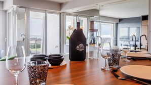 Mesa de comedor dispuesta con varios vasos y una botella etiquetada "LSO PASSION" en una cocina moderna con ventanas amplias.