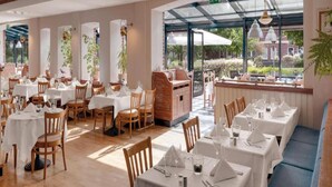 A restaurant with multiple tables and chairs, a grill station, and large windows offering a view of the outdoors. - Sunday Resort Rugen Double Room Disability Access (Sagard)