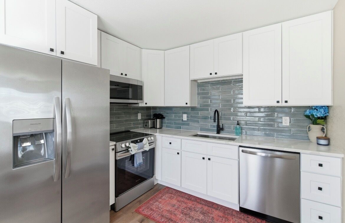 Una cocina moderna con armarios blancos, electrodomésticos de acero inoxidable y salpicadero de azulejos.