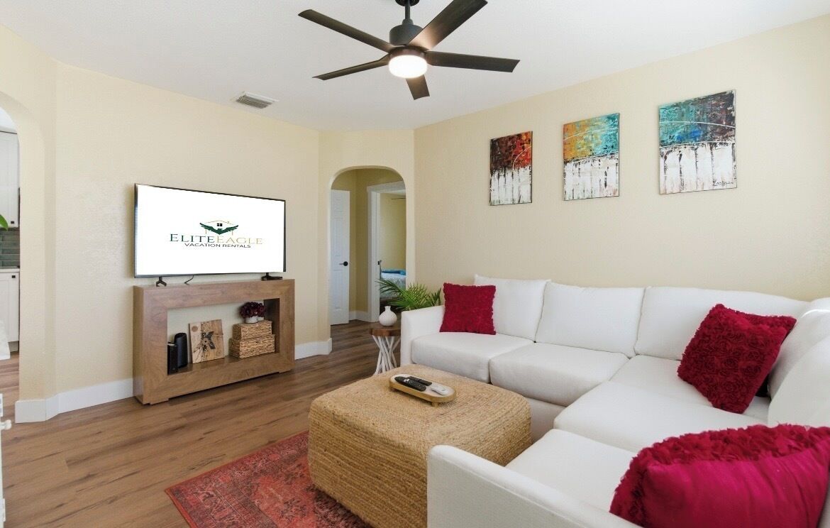 Una sala moderna con un sofá blanco, cojines rojos, una consola de madera, un televisor de pantalla plana y arte abstracto en la pared.