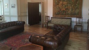 Un salon avec un canapé en cuir marron, un fauteuil à motifs et une grande tapisserie accrochée au mur.