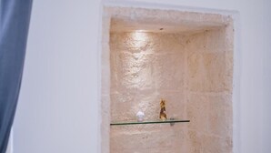 Ett litet, avgränsat utrymme med en vägg som har en intressant yta, en hylla av glas och en liten statyett.