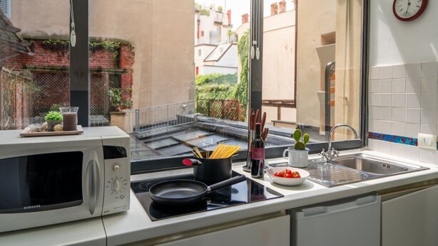 Une cuisine équipée d’un four à micro-ondes, d’une cuisinière, d’un évier et d’une fenêtre donnant sur une cour.