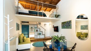 Un appartement moderne de style « loft », doté d’un lit en mezzanine, d’un coin repas avec une table en verre et d’un escalier menant à l’étage supérieur.
