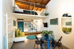 Eine moderne Loft-Wohnung mit Schlafgalerie, einem Essbereich inklusive Glastisch und einer Treppe zur oberen Ebene.