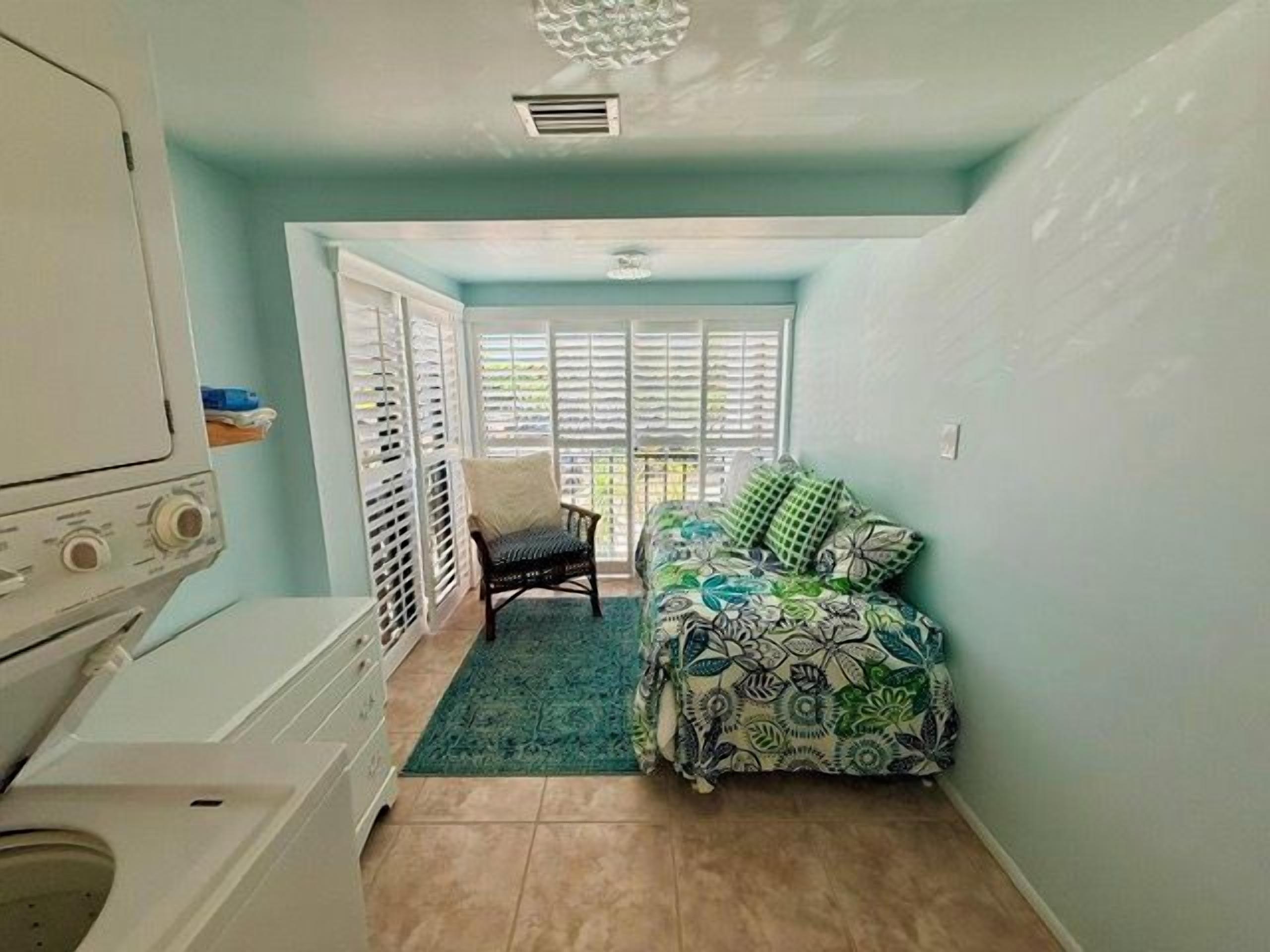 A room with a bed, a chair, a washing machine, and a window with blinds.