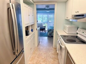 A compact kitchen with a refrigerator, microwave, stove, and white cabinets. - Walk-Out Beachfront Condo | Sleeps 7 | Heated Pool | Old Florida Charm (Longboat Key)