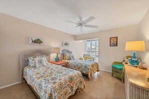 A bedroom with two beds, a ceiling fan, and a window with blinds. - Walk-Out Beachfront Condo | Sleeps 7 | Heated Pool | Old Florida Charm (Longboat Key)