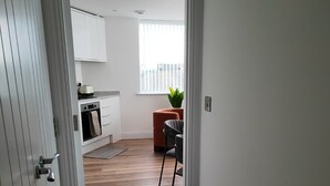 Corredor que dá para uma cozinha com piso de madeira, um capacho e uma planta.