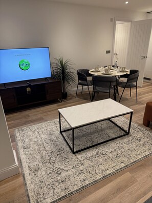 Un salon moderne comprenant un téléviseur, une table à manger avec des chaises, une table basse et un tapis à motifs.