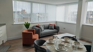 Uma sala de estar moderna com um sofá cinzento, uma poltrona laranja e uma mesa de jantar posta para quatro pessoas.