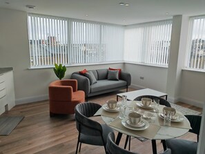 A modern living room with a grey sofa, orange armchair, and a dining table set for four. - The Cosy Quayside Apartment - Two bedroom/Parking (Gravesend)