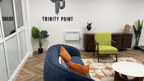 Um espaço de escritório moderno com uma poltrona de tecido azul, uma poltrona verde e uma mesa branca. Um logotipo grande na parede diz "TRINITY POINT".