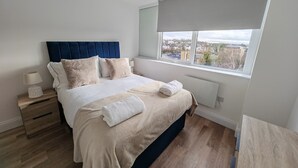 Quarto moderno com uma cama grande, uma mesa de cabeceira, uma janela com vista para a cidade e um radiador.