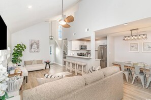 A spacious living area with a sofa, a dining table with chairs, a kitchen area with a microwave and refrigerator, and a ceiling fan. - Walk to Beach, Pool, King Suite, Sleeps 8 (North Myrtle Beach)