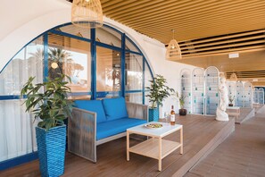 A modern lounge area with a blue sofa, wooden flooring, and a white table with a plate of fruit and a bottle.