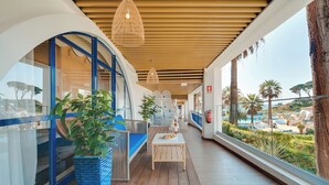 Un couloir avec un plafond en bois, un coin salon avec une table, et une vue sur une piscine et des palmiers.