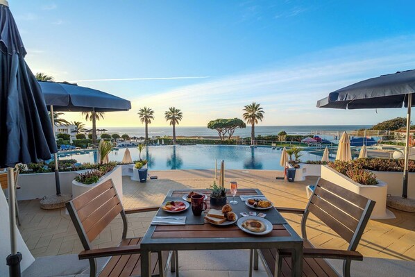 A dining table with plates of food, a bottle, and a glass of water, overlooking a pool and the ocean.
