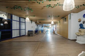 A corridor with wooden slats on the ceiling, hanging plants, and a Buddha statue.