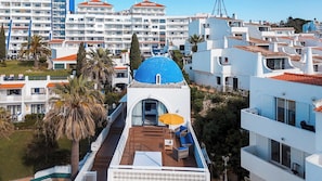 A rooftop terrace with a blue dome, white buildings, and palm trees.