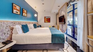 Une chambre d’hôtel moderne avec un grand lit, un papier peint à motifs floraux, un bureau avec un téléphone et une fenêtre avec des rideaux.