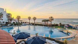 A resort pool with palm trees, lounge chairs, and umbrellas. - Monicca Collection Oura View Suites (Albufeira)