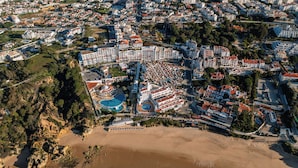 Vue aérienne d’une station balnéaire comprenant plusieurs bâtiments, une grande piscine et une plage.