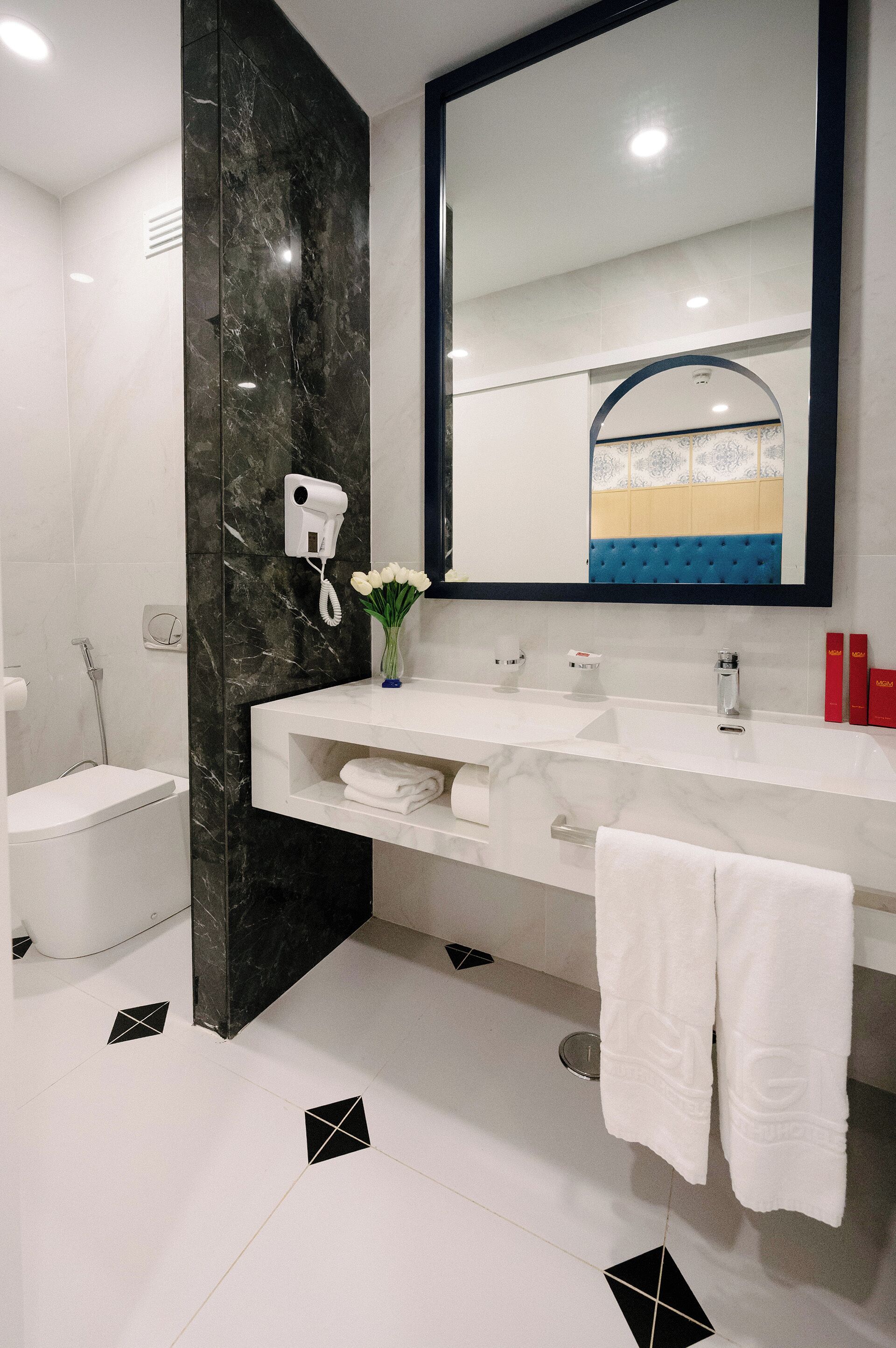 A modern bathroom with a white sink, black marble accent wall, a large mirror, and a towel rack.