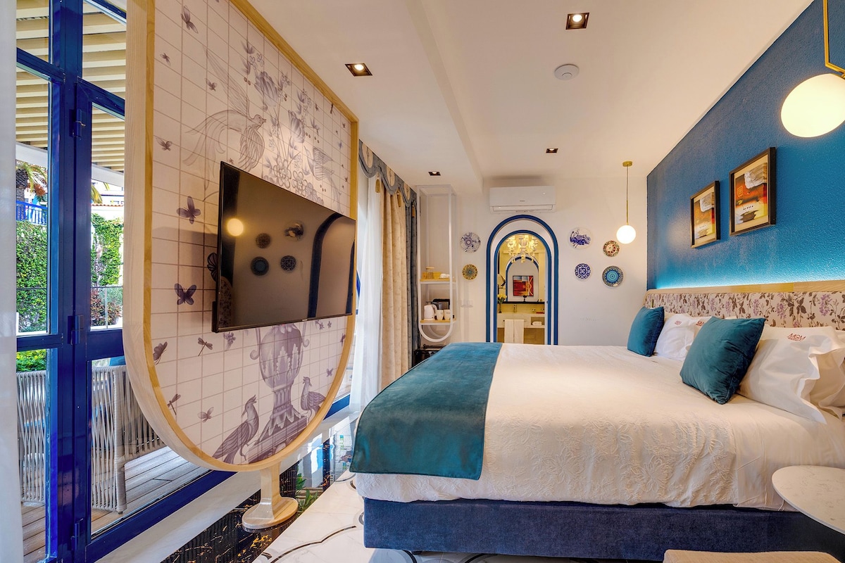 A modern bedroom with a large bed, a TV mounted on the wall, and a view of the outside balcony.