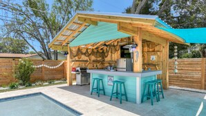 Une cuisine extérieure en bois, avec une piscine, des tabourets de bar et un panneau indiquant une autoroute à proximité.