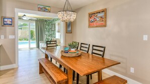 Un espace repas avec une table en bois, des bancs et un lustre. Des chaises sont disposées autour de la table, et une plante est posée sur la table.