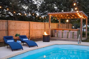 A backyard with a swimming pool, two lounge chairs, a tiki bar, and a wooden fence. - Seaside Villa (St. Augustine)