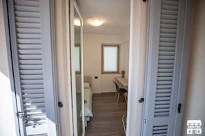A narrow hallway with a bed, a desk, and a chair in a small room.