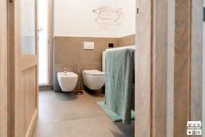 Ein schmaler Flur, der zu einem Badezimmer mit Bidet, Toilette und Handtuchhalter führt.