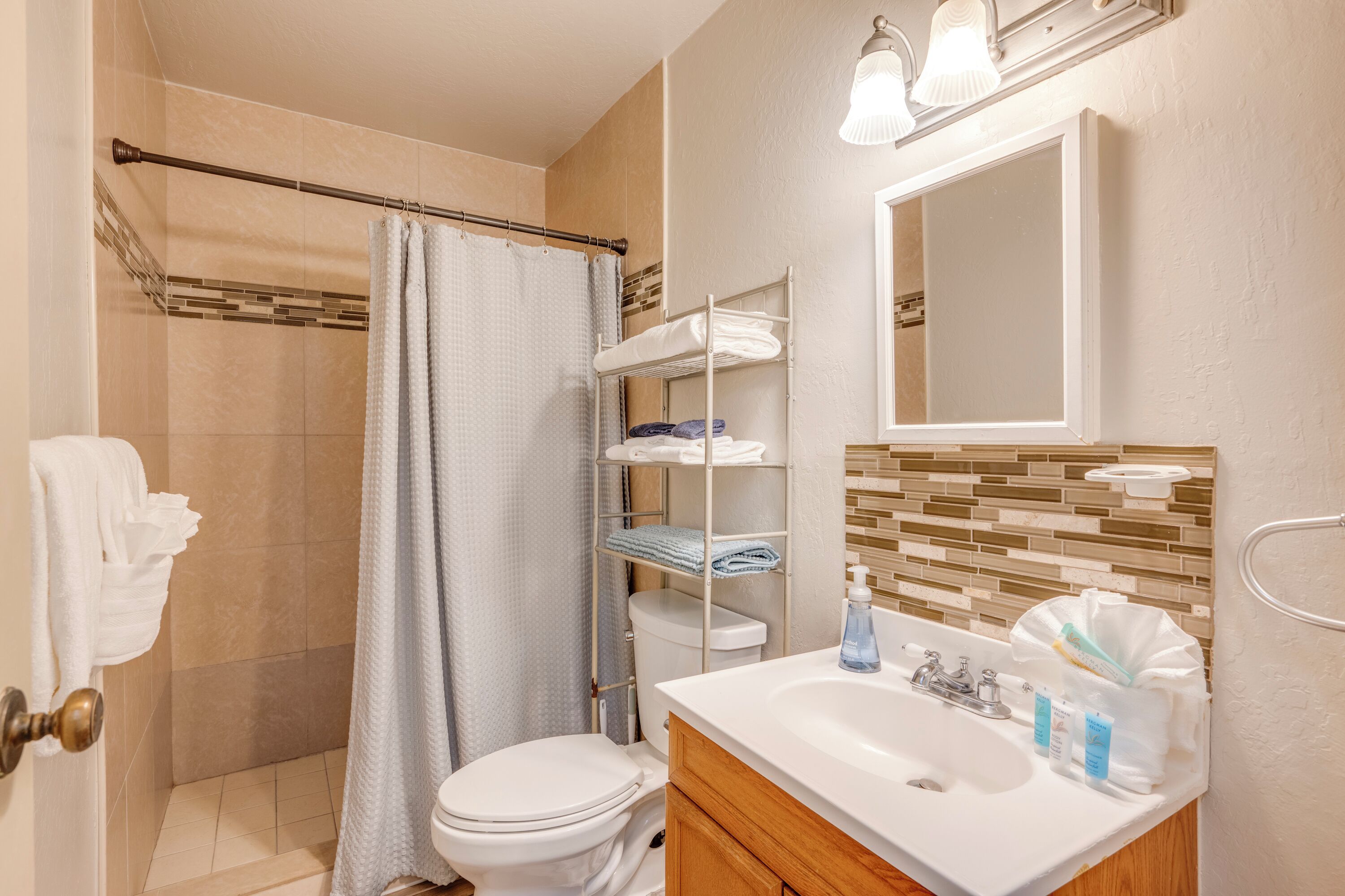 A bathroom with a shower, toilet, and sink. There are shelves with towels and toiletries.