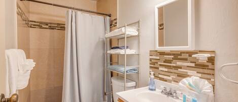A bathroom with a shower, toilet, and sink. There are shelves with towels and toiletries.