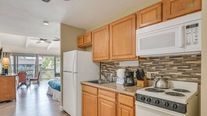 A kitchen with wooden cabinets, a microwave, a stove, and a refrigerator. - Kihei Bay Surf B212: Beachside Studio w/ Pool & Lanai (Kihei)