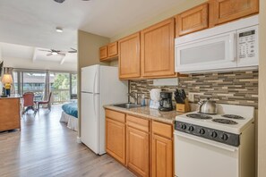 A kitchen with wooden cabinets, a microwave, a stove, and a refrigerator. - Kihei Bay Surf B212: Beachside Studio w/ Pool & Lanai (Kihei)