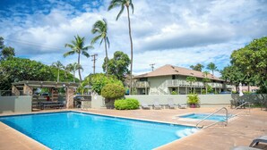 A swimming pool with lounge chairs and a covered seating area, surrounded by palm trees and a building with balconies. - Kihei Bay Surf B212: Beachside Studio w/ Pool & Lanai (Kihei)