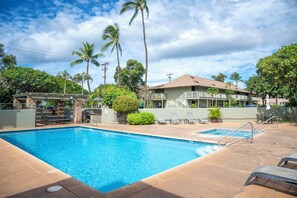 A swimming pool with lounge chairs and a covered seating area, surrounded by palm trees and a building with balconies. - Kihei Bay Surf B212: Beachside Studio w/ Pool & Lanai (Kihei)