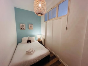 A bedroom with a bed, a bedside lamp, a wall-mounted picture, and a wardrobe. - Le Millésime Barbatre | Centre-ville | 7 couchages (Reims)