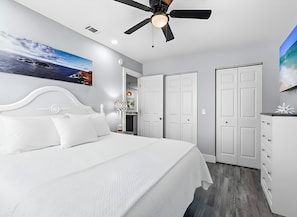Un dormitorio con cama, ventilador de techo, un cuadro de una playa y un armario.