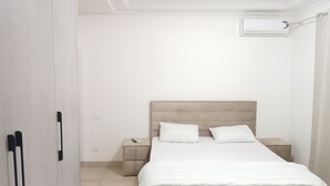 Ett minimalistiskt sovrum med en säng, sängbord och en luftkonditioneringsanläggning.