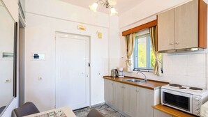 Cocina compacta con microondas, estufa y pileta, una mesa de comedor con sillas y una puerta con un ventanal.