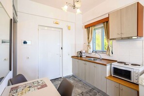 Et lille køkken med mikroovn, komfur og vask, et spisebord med stole, samt en dør med et lille vindue.