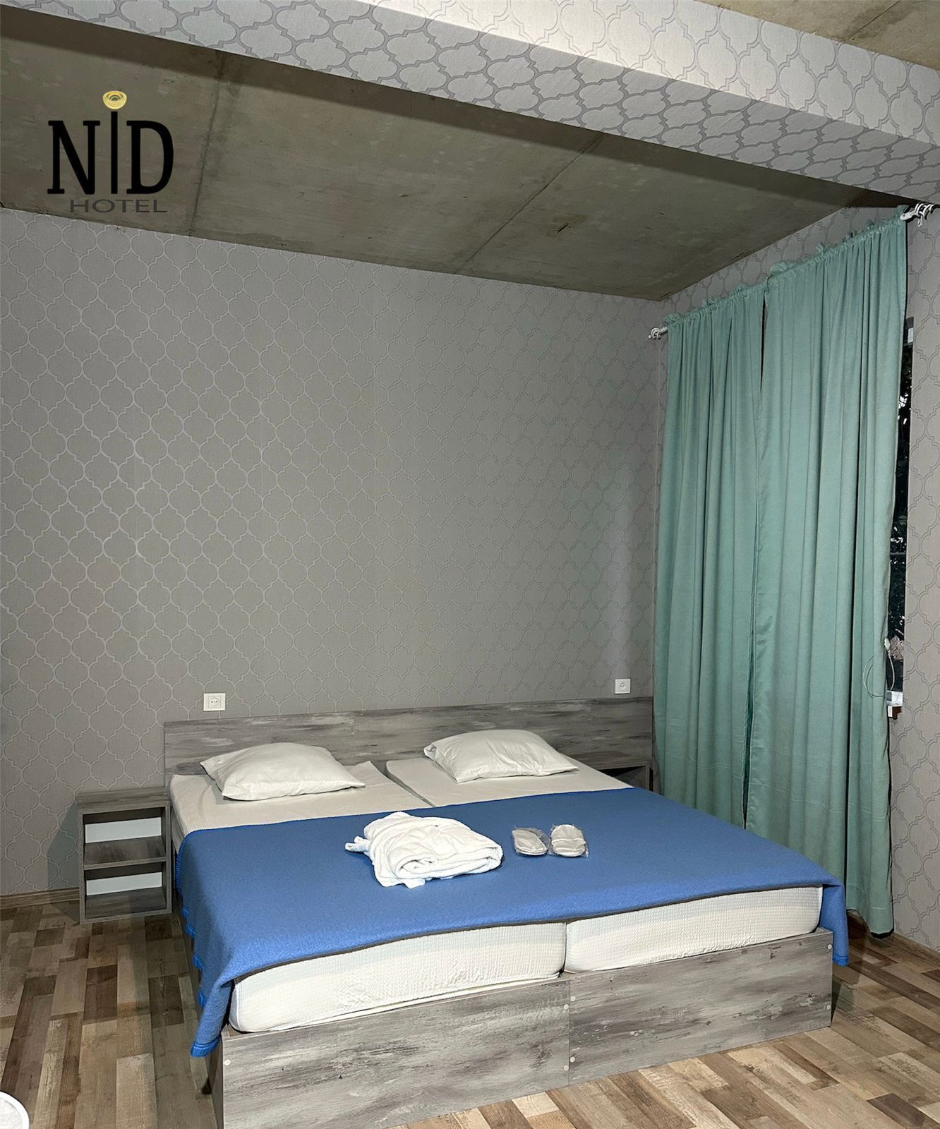 A hotel room with a bed, a nightstand, and a window with curtains.