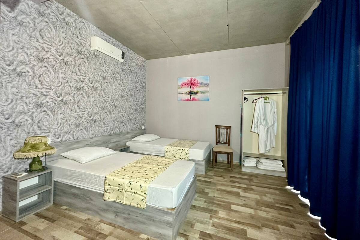 A hotel room with two beds, a wooden floor, a painting, a chair, and a robe rack.